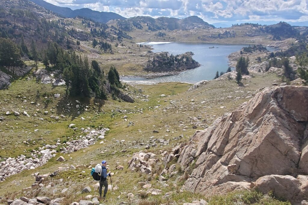 A woman hikes off trail through alpine scenery