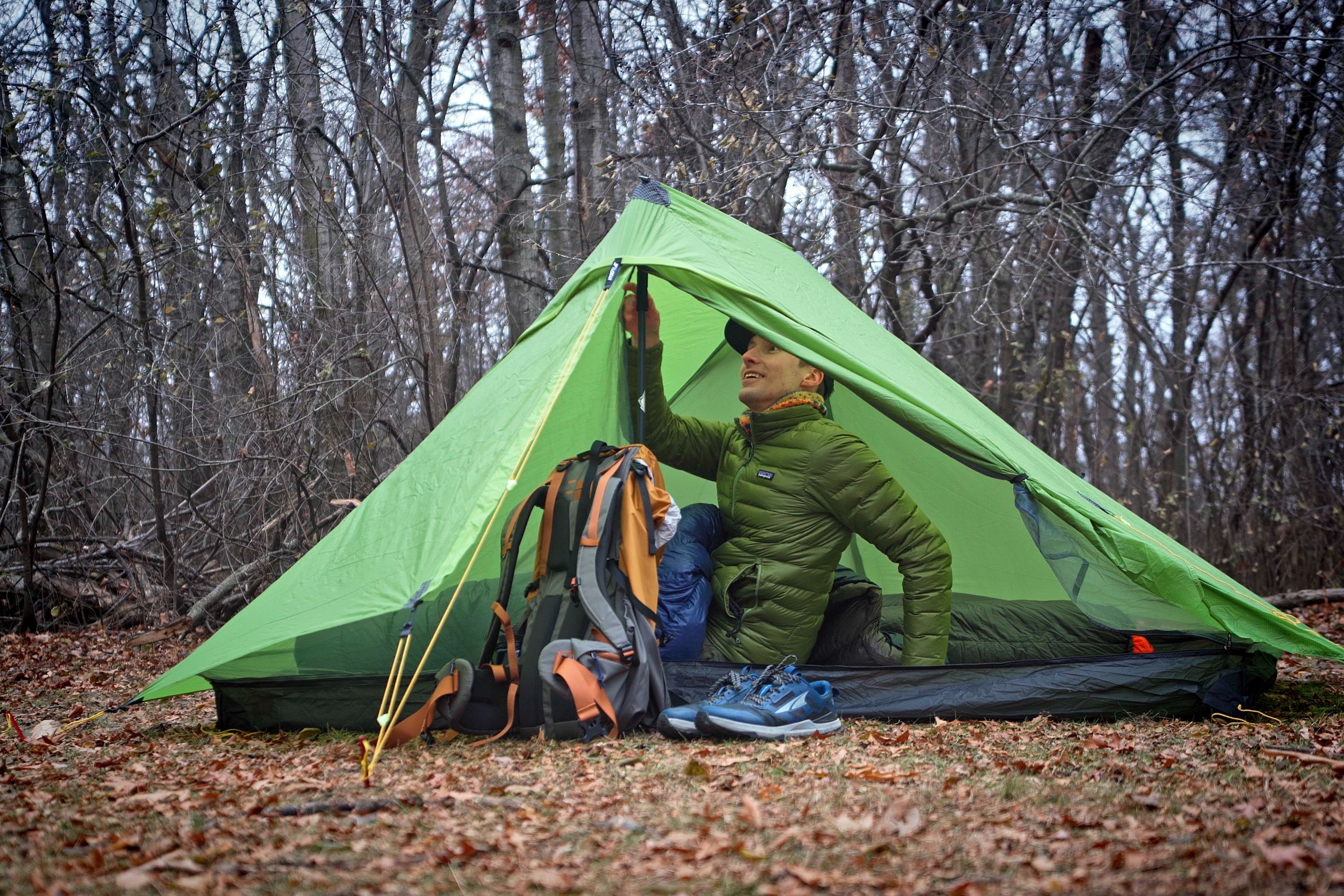 a man in a green coat sits inside of a green tent