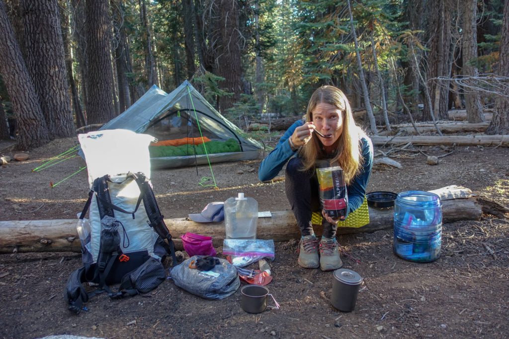 A backpacker eating a freeze-dried meal at a campsite