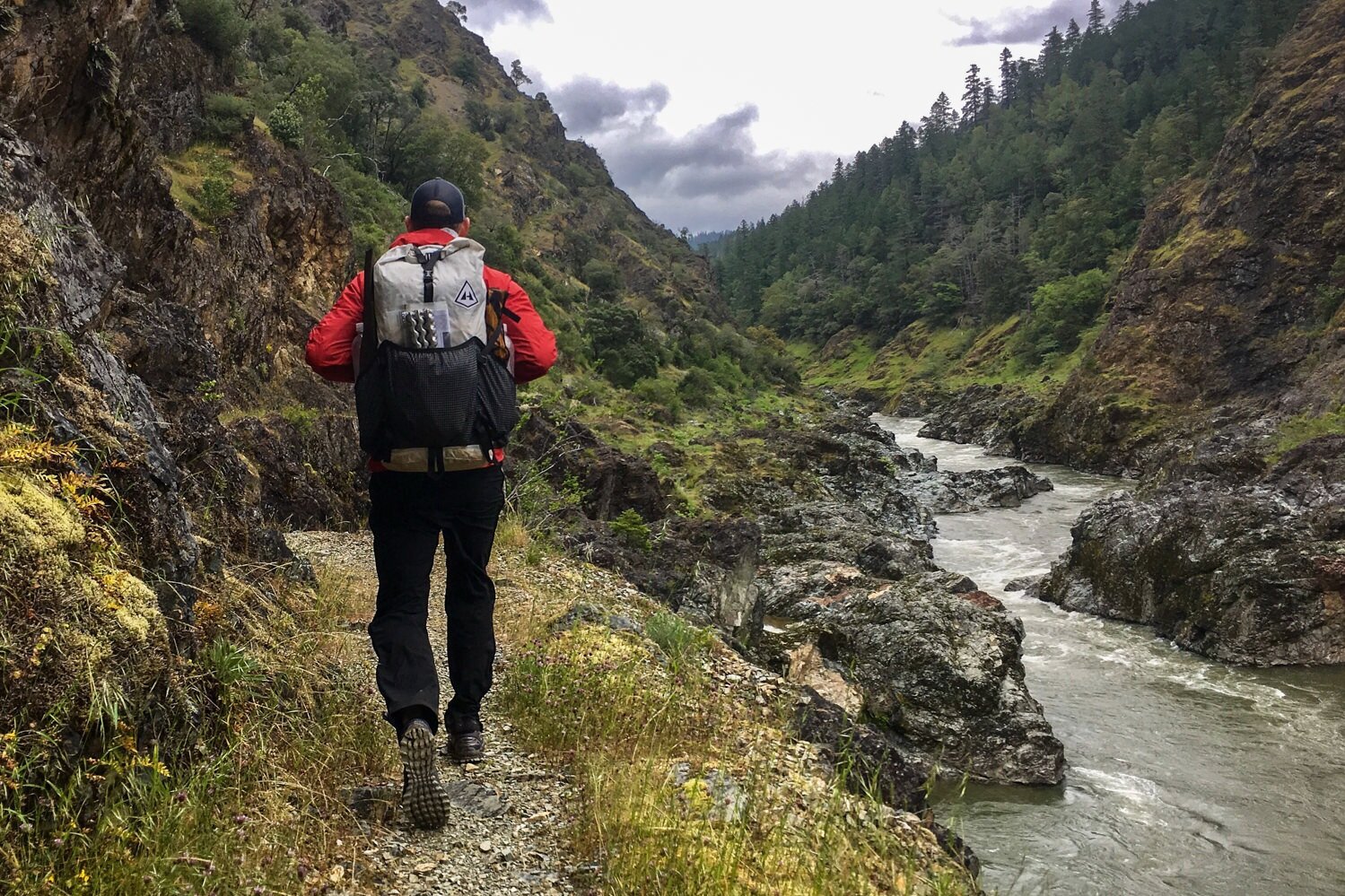 hiker walking on a mossy trail next to a river on a wet day