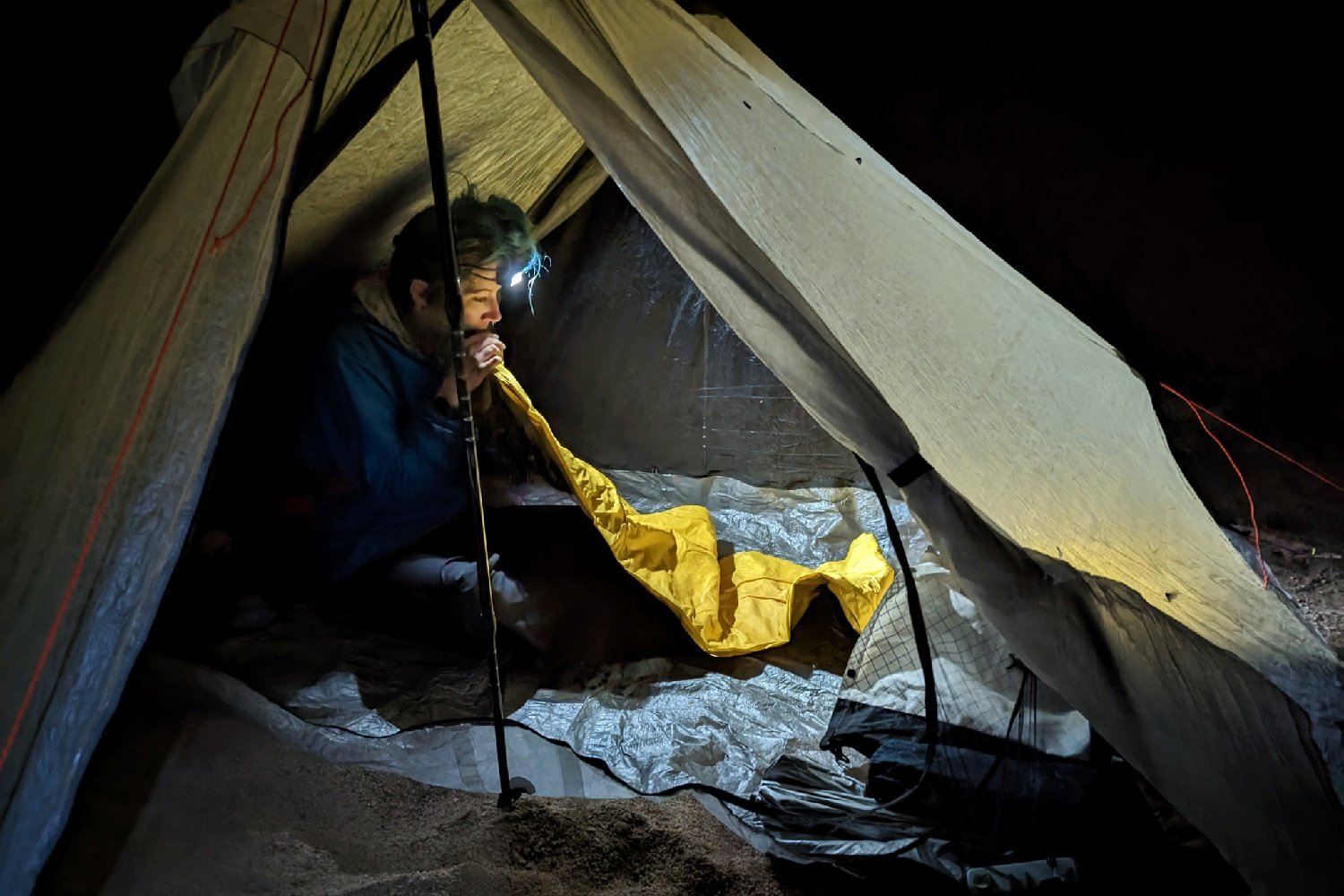 a backpacker is inflating their sleeping pad while inside their tent. the image is lit by their headlamp light