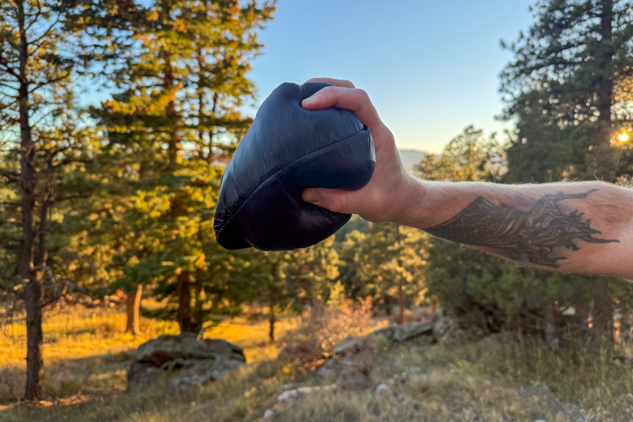 The packed-down jacket is shown compressed into a small bundle, demonstrating its ultralight and highly compressible design.