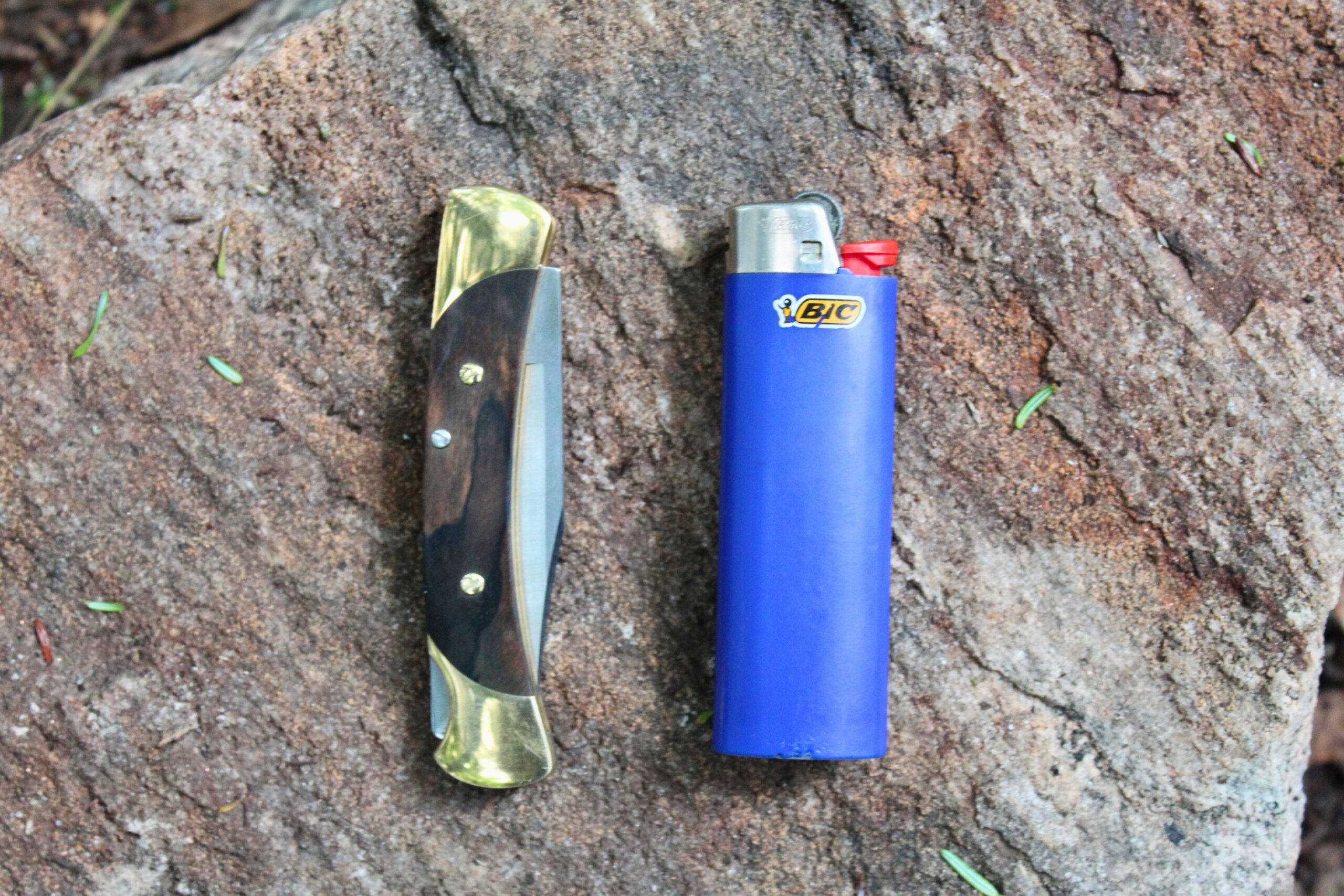 The Buck Knives 055 Pocket Knife next to a BIC lighter on a rock