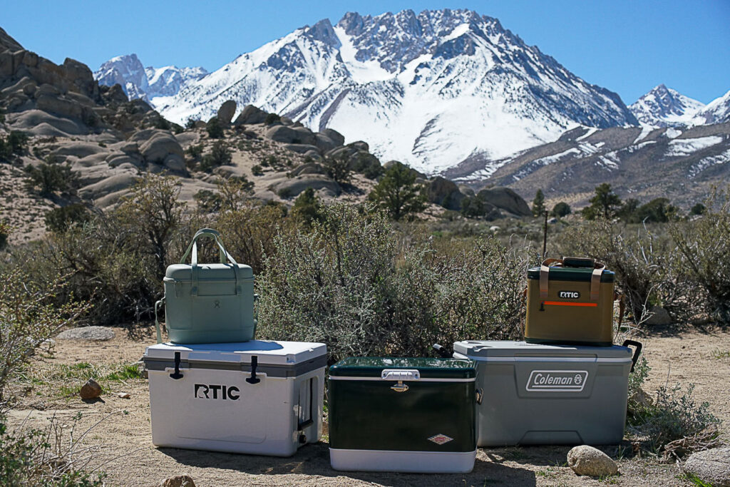 The Hydro Flask Carry Out 20L sits on top of the RTIC Ultralight 52. The Coleman Steel Belted cooler is in the middle, with the RTIC Soft Pack sitting on top of the Coleman 316 Series 70QT to the right.