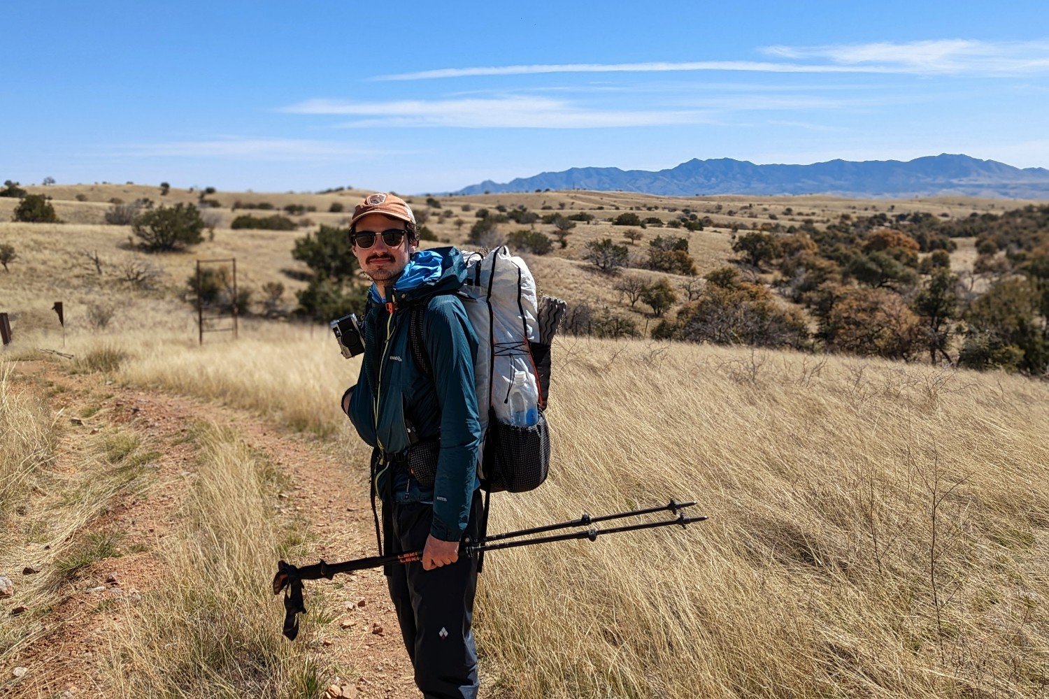 a man holding trekking poles in a high prairie dirt road