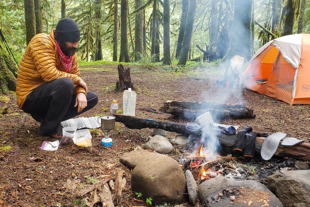 backpacker tending fire in a rainforest campsite