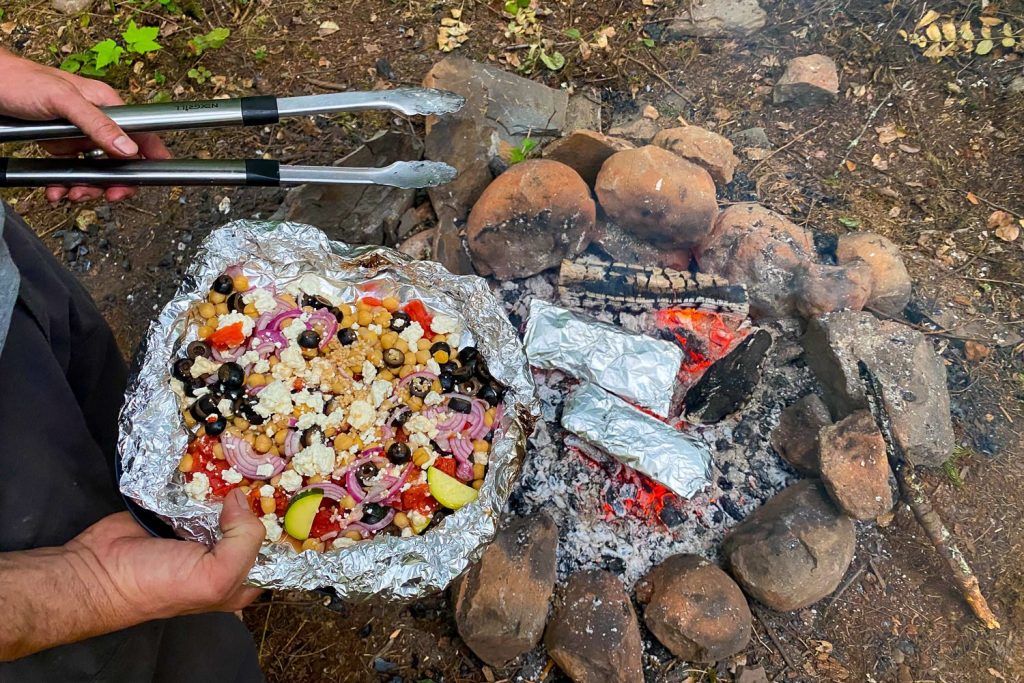 foil packet campfire meal cooking in the fire and one in a person's hand unwrapped