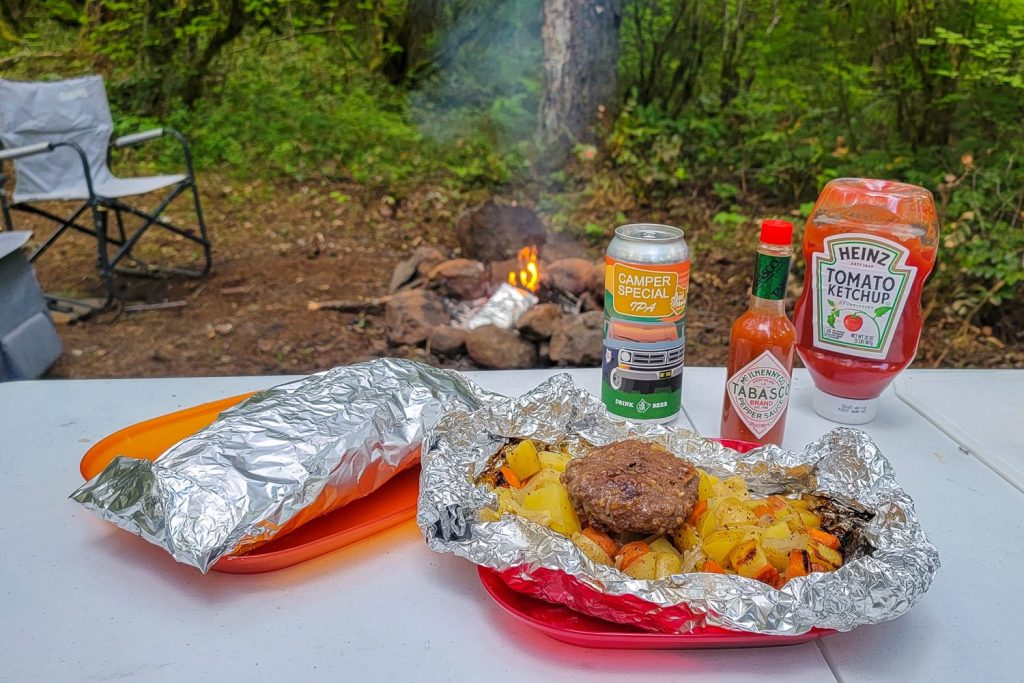 food cooked in a foil packet on a table with sauces and drinks