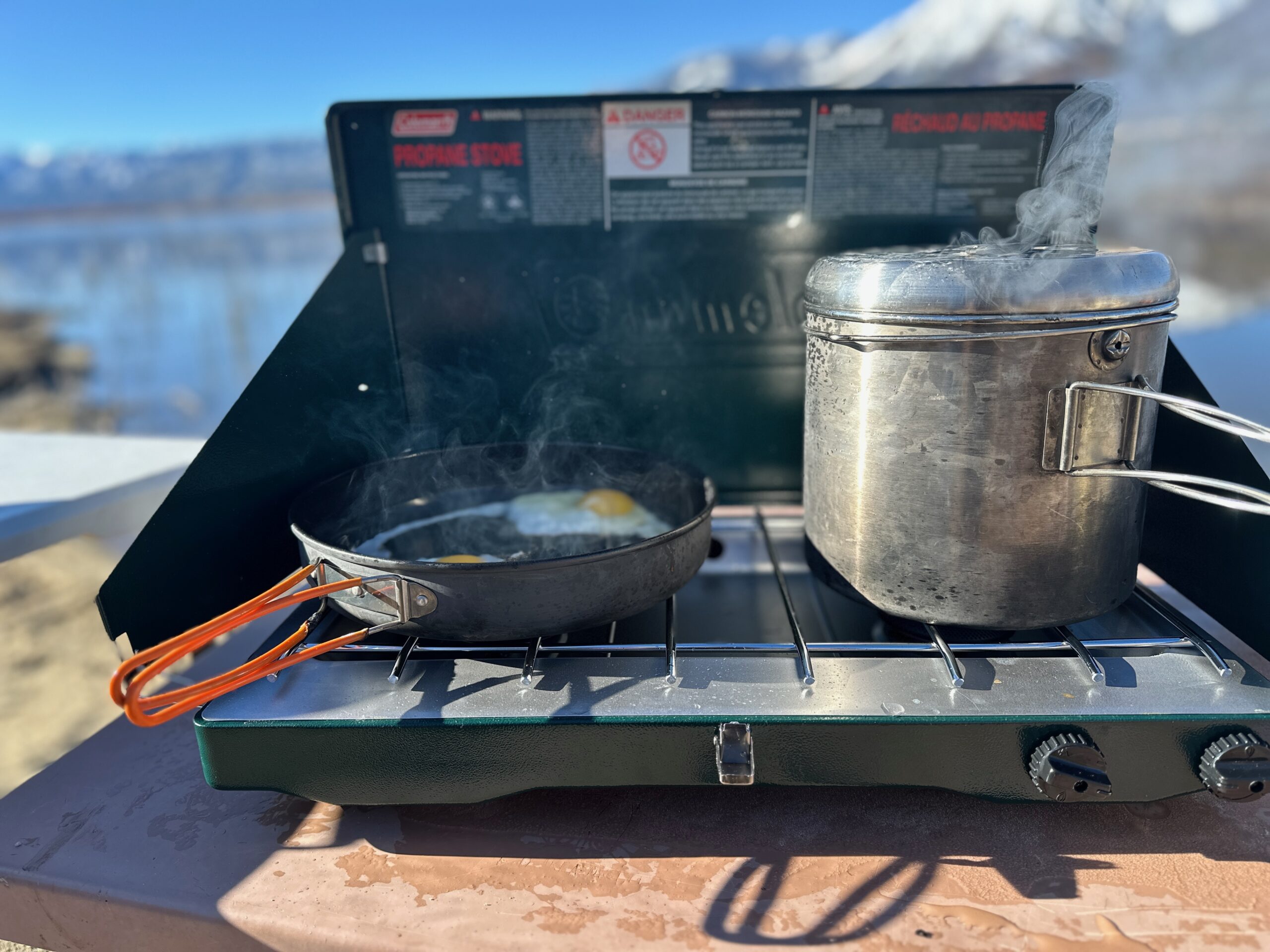 the Coleman Classic 2-Burner cooking camp meals at a beachside camp