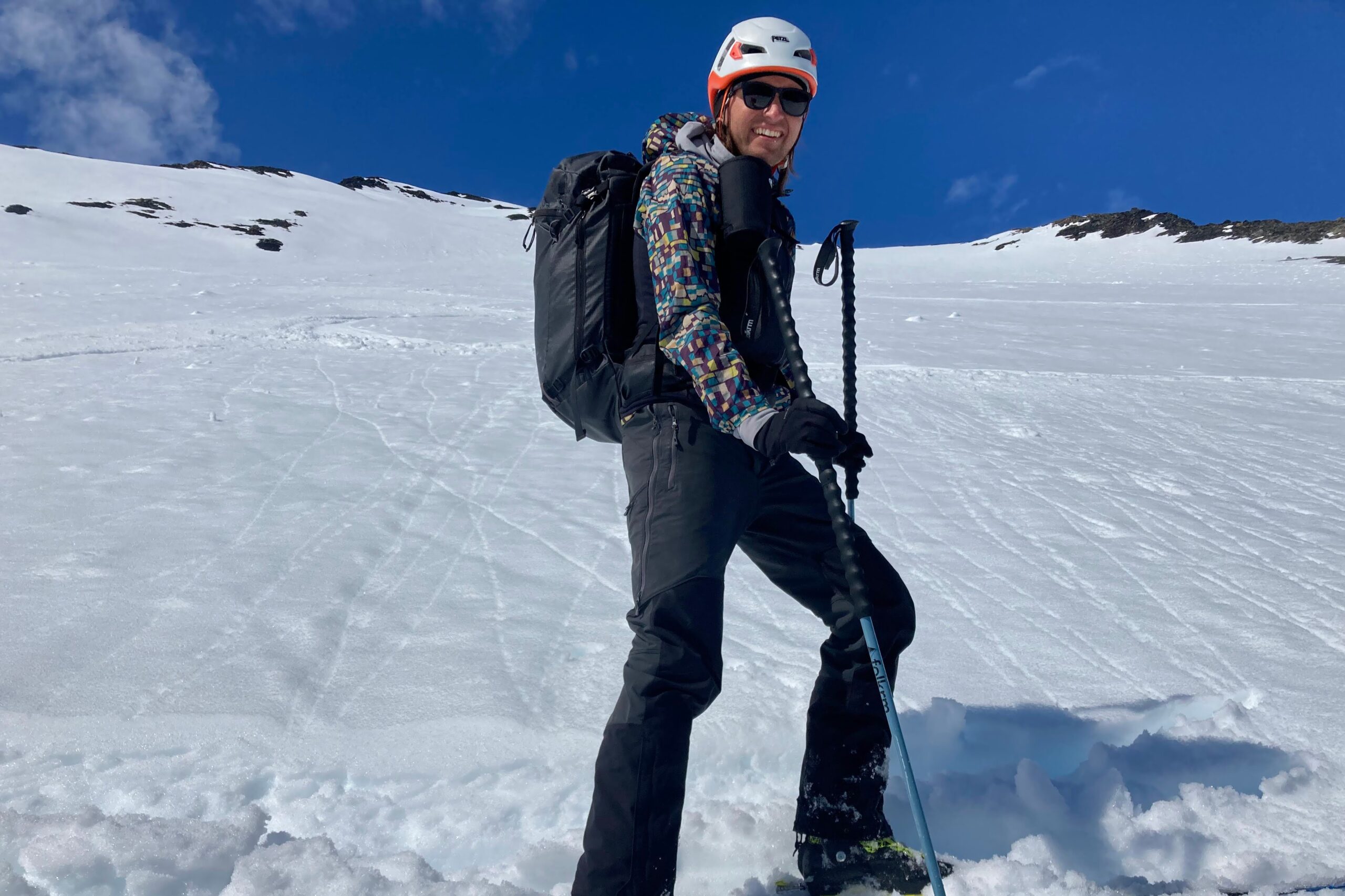 A man stands on a snowy mountainside wearing a purple jacket.
