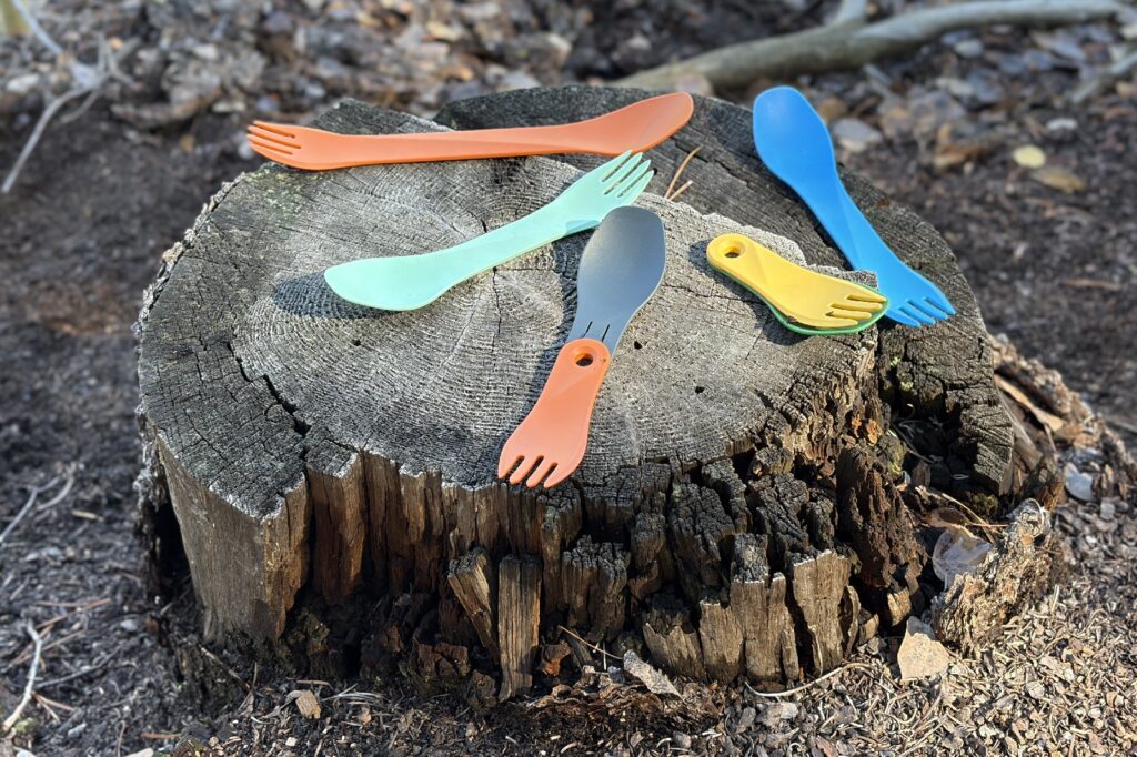 a variety of plastic sporks rest on a tree stump