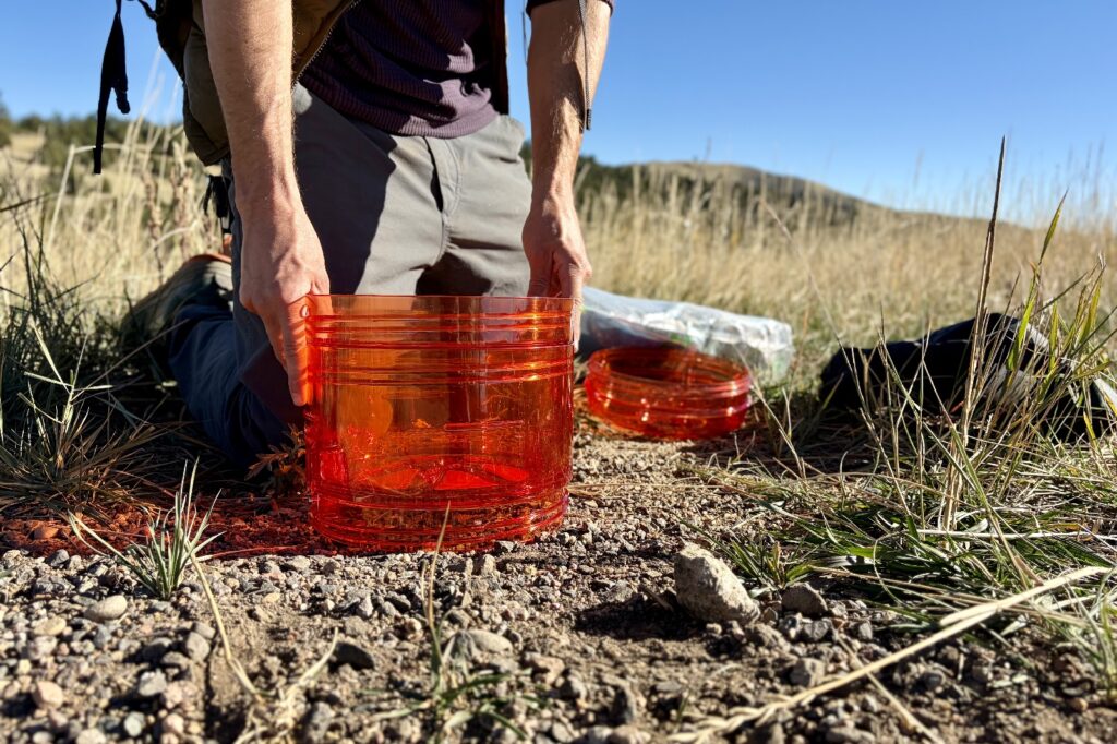 a hiker kneels to nest two parts of an orange bear canister together