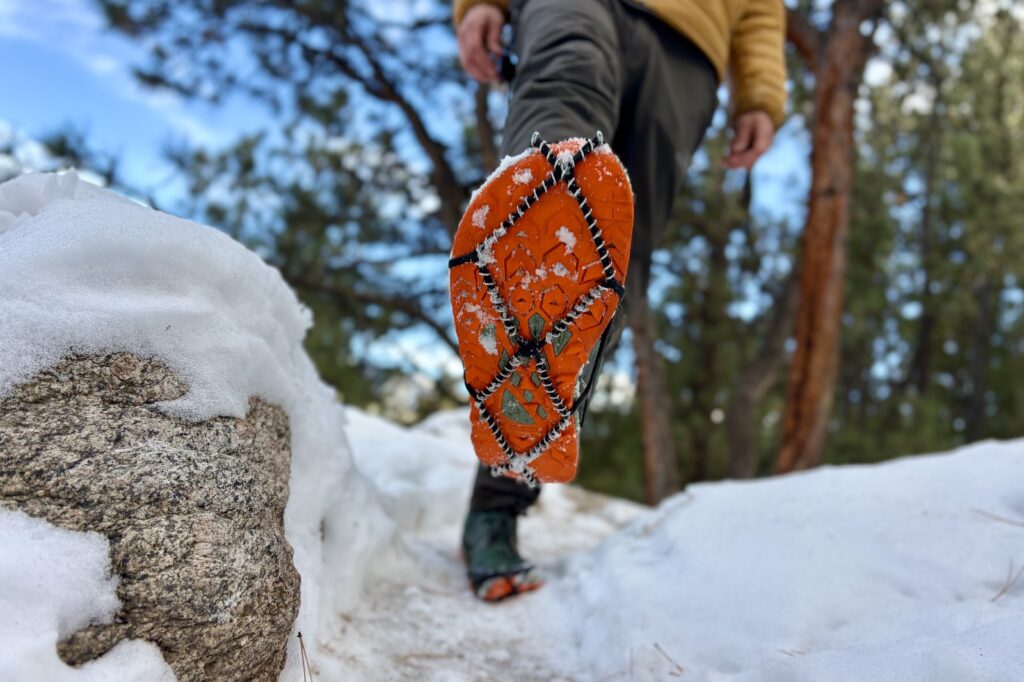 a hiker walks towards the camera showing the bottom of one shoe with a traction device attached