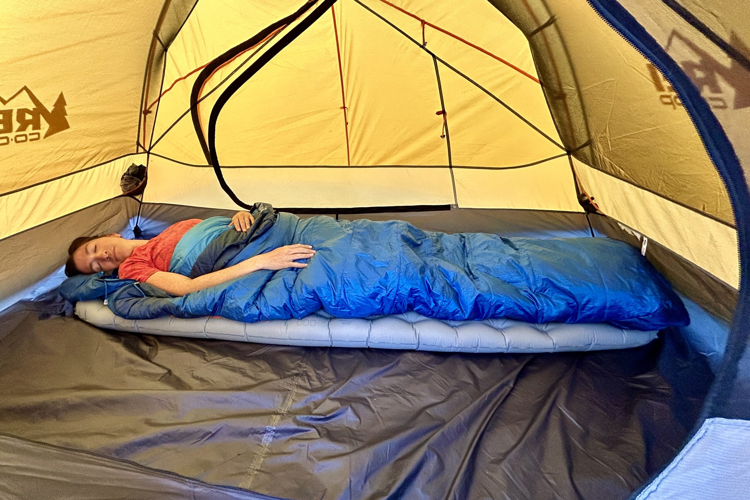 A person lies asleep in a tent, cozy in a sleeping bag on a thick air pad.