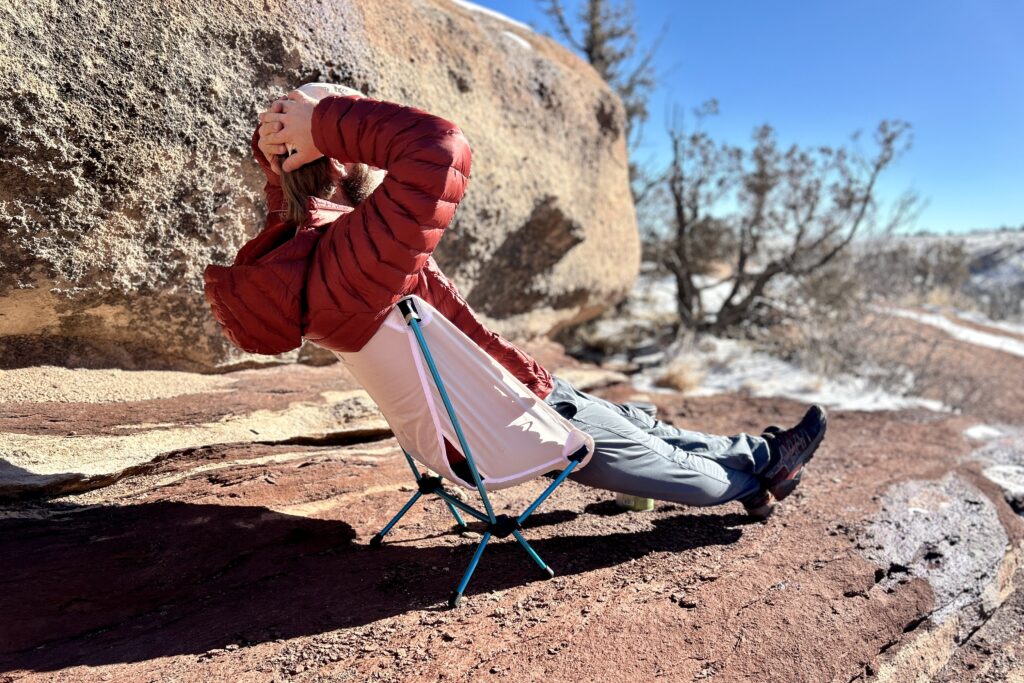 A man relaxes with his legs out and hands behind his head on a small backpacking chair.