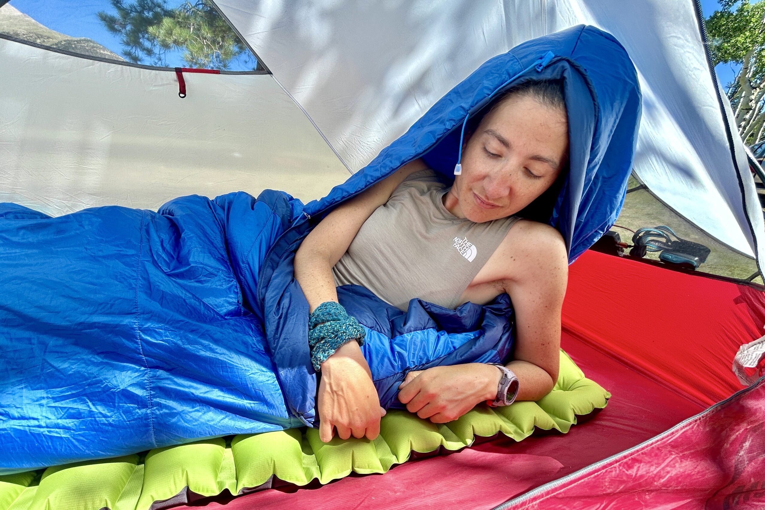 A close-up image of a woman waking up in a tent in the Marmot Trestles 20 sleeping bag in a red tent in the sun.