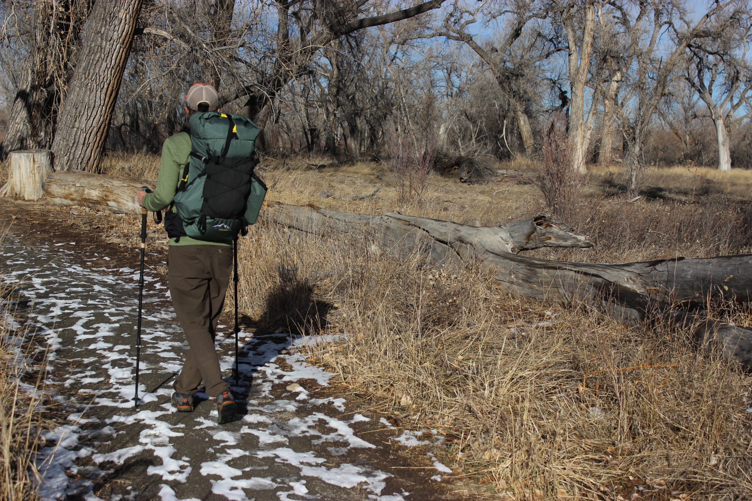 A hiker walks away from the camera wearing the ULA Circuit backpack and trekking poles