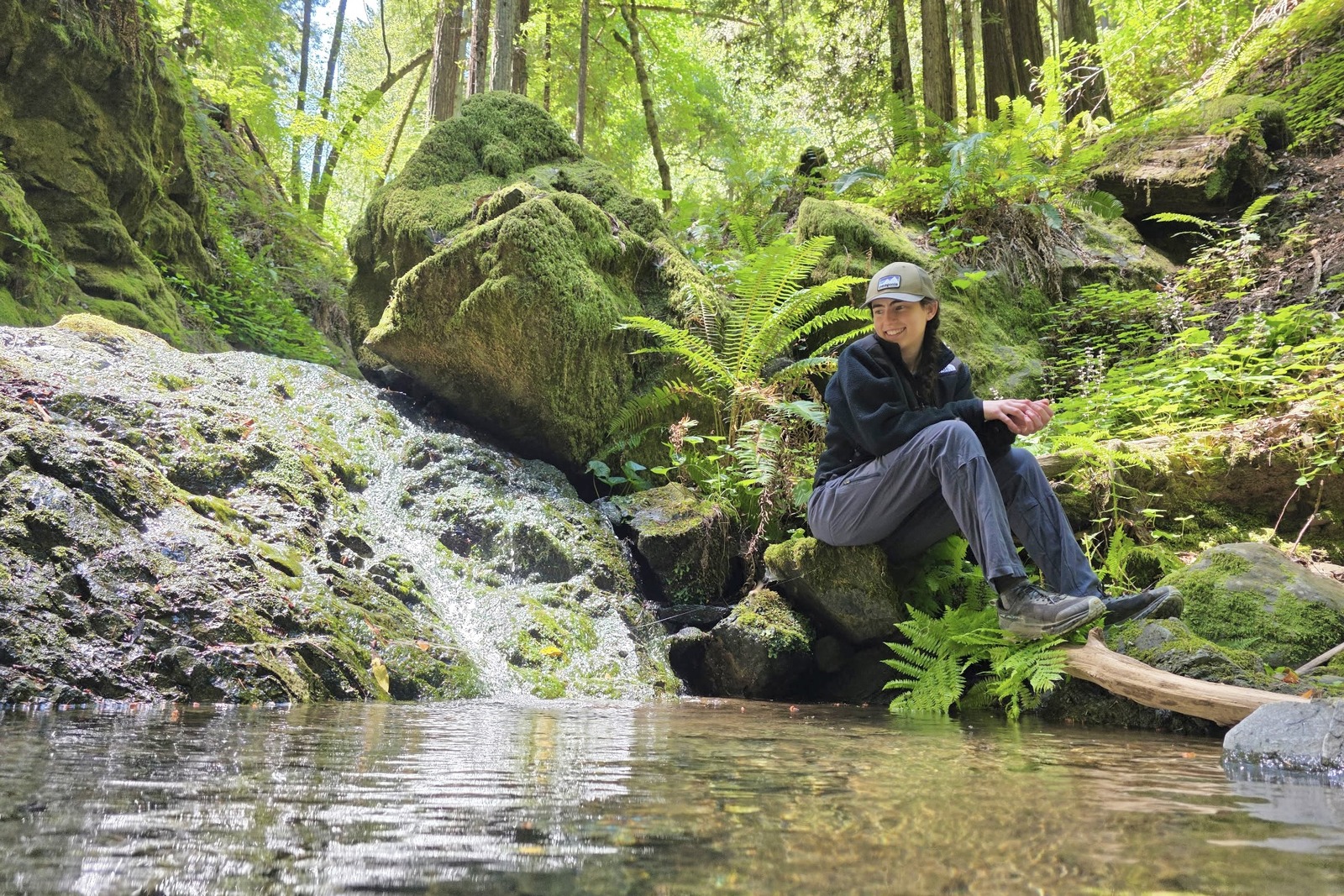 Woman sits next to a creek, cozied up in the Retro Denali Fleece.