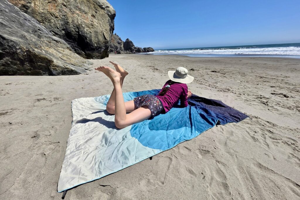A woman lays on a blanket at the beach.