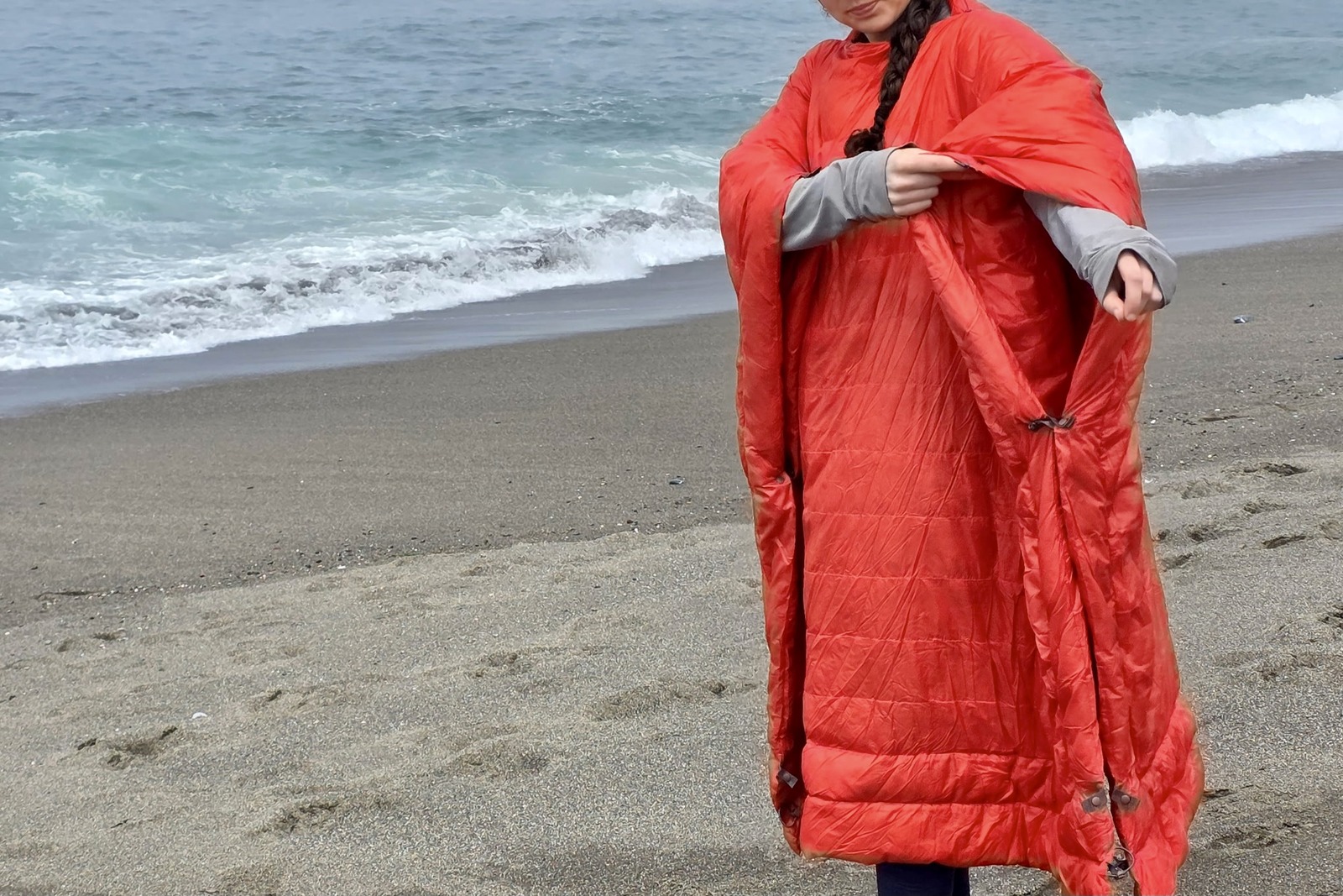 A woman stands on the beach in her poncho.