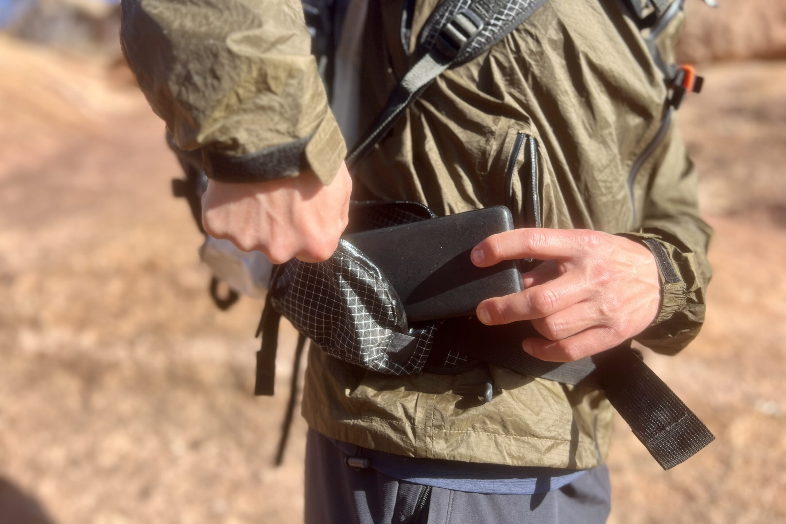 A hiker pulls a battery pack from the hipbelt pocket of the Southwest 55 pack with a desert background.