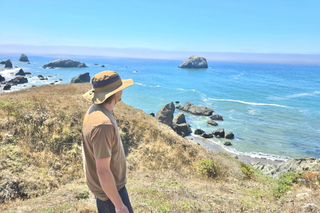A man stands on a hill overlooking the Pacific Ocean.