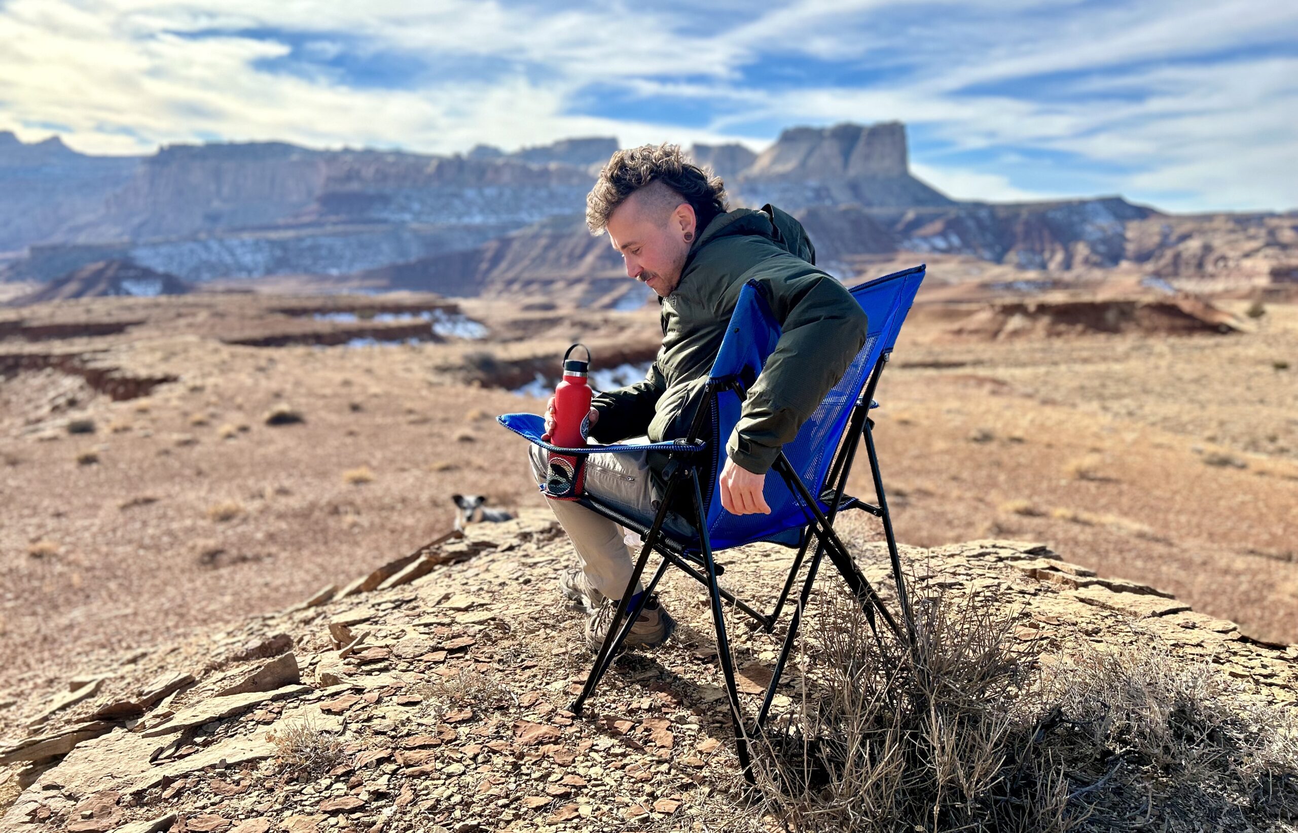 A man sits in a camping chair in a sunny desert setting.