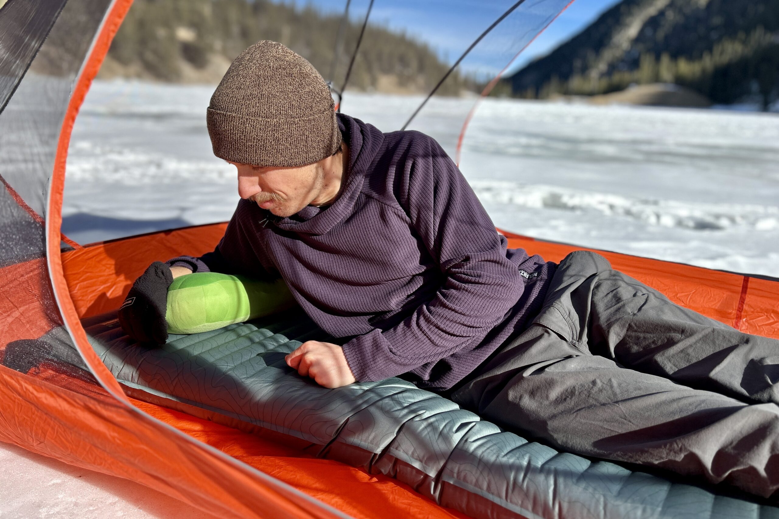 A man rests on a sleeping pad in a tent in a wintry setting.