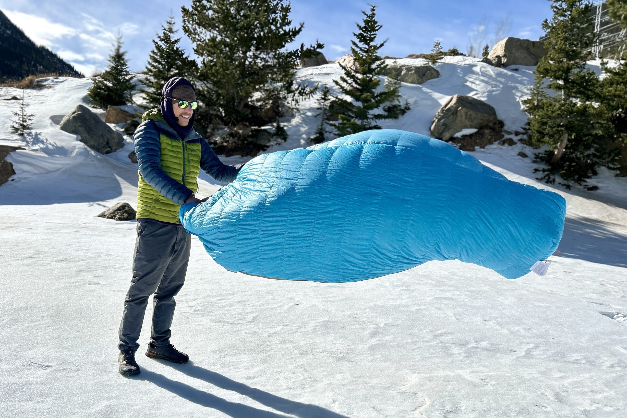 A man fluffing a sleeping bag in a bright, wintry setting.