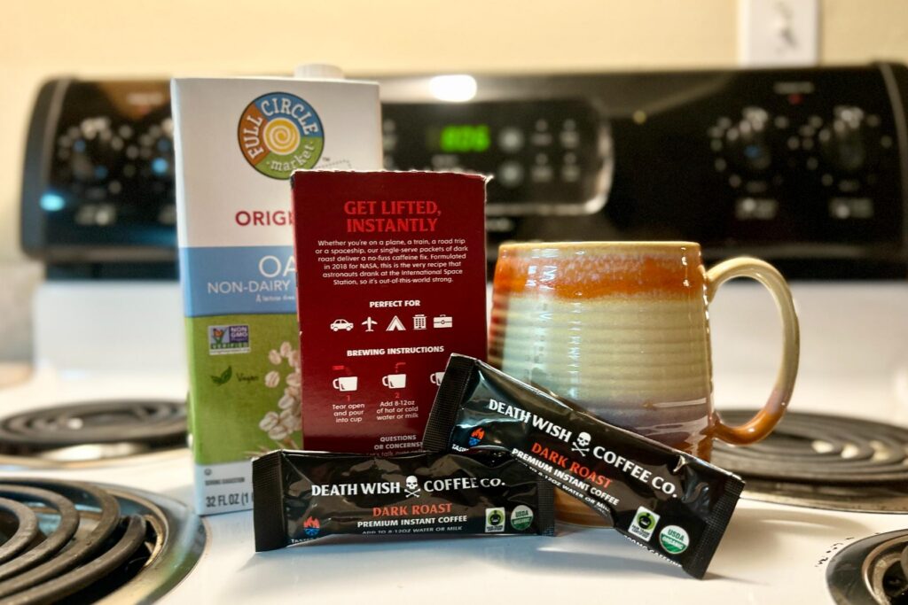 Up-close image of a box of Death Wish instant coffee staged in front of a mug and a small box of oat milk on top of a stove.