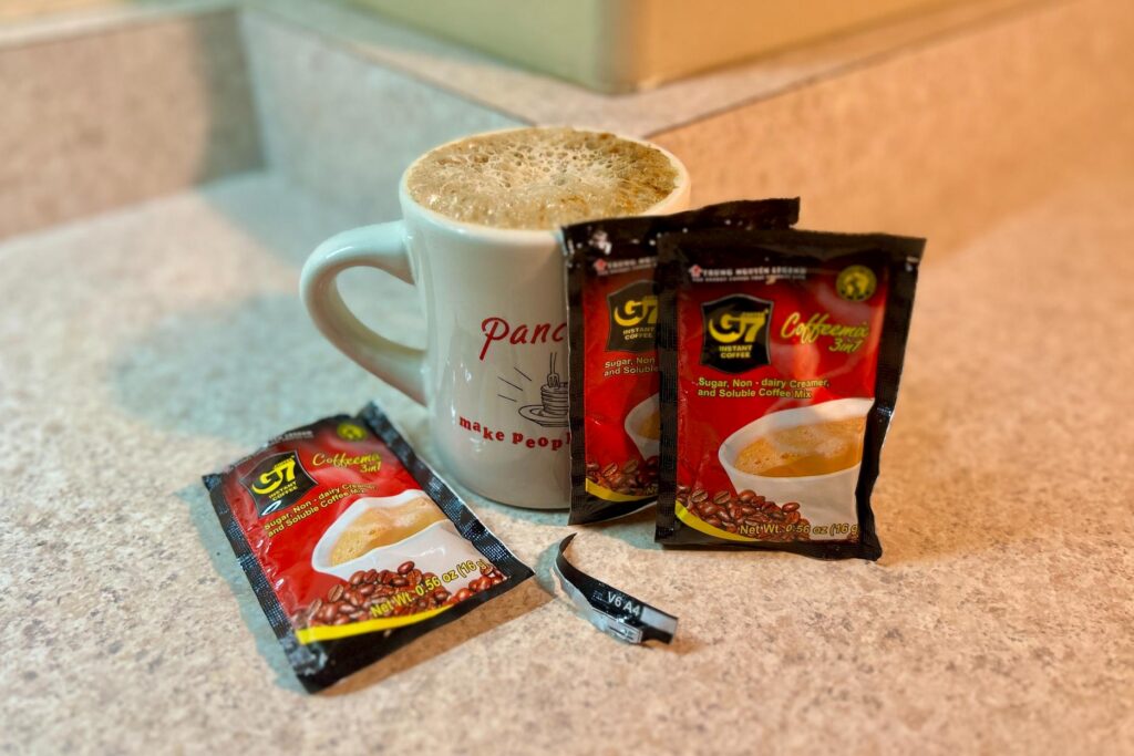Up-close image of a few packets of G7 Vietnamese coffee next to a mug of frothy coffee.