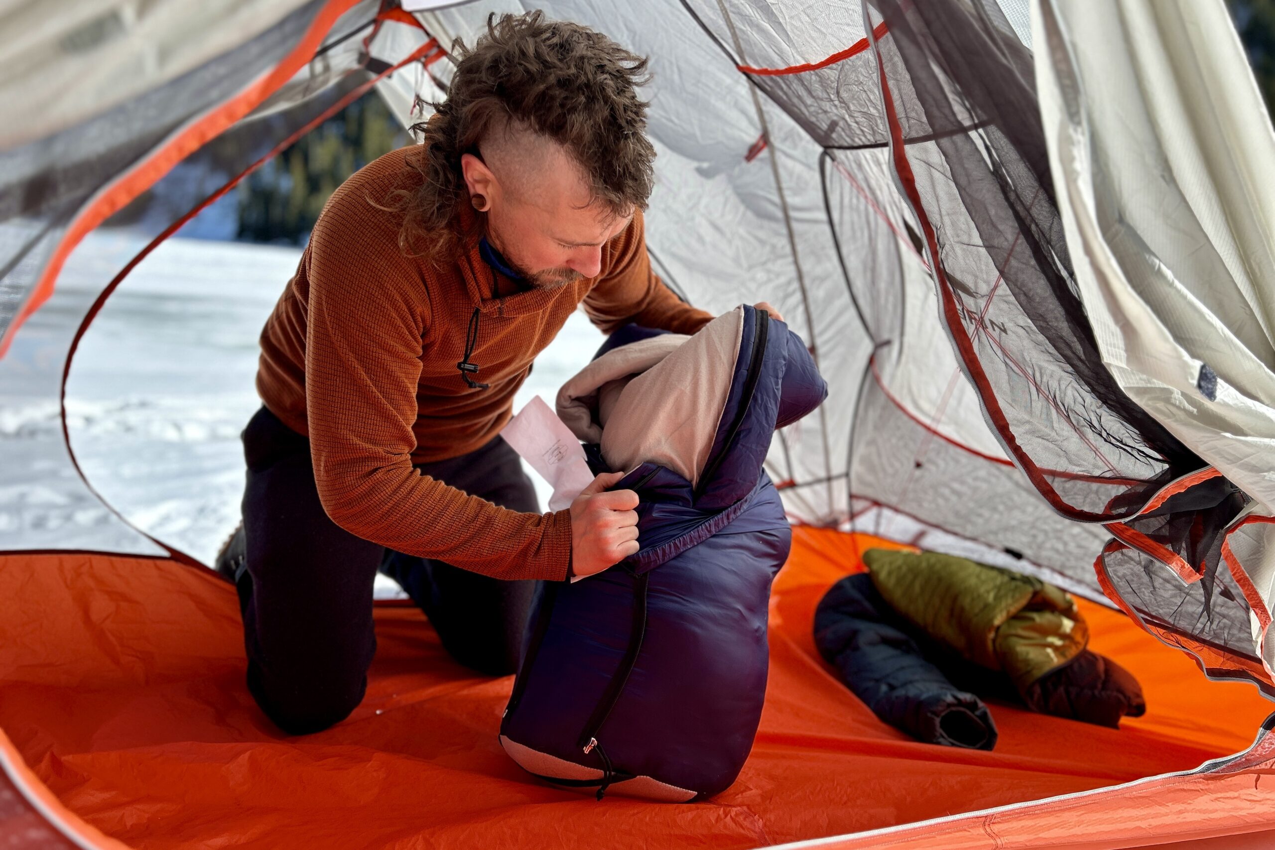 A man stuffs a sleeping bag into a stuff sack in a camping tent.