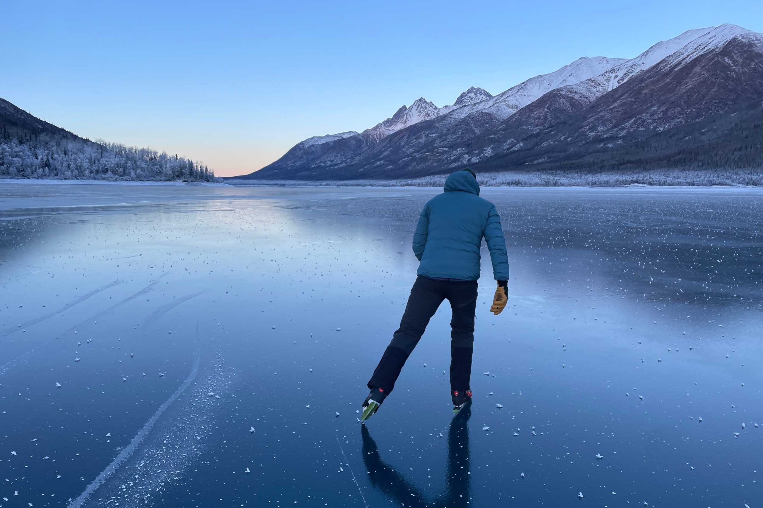 A man ice skates away from the camera under a blue sky.