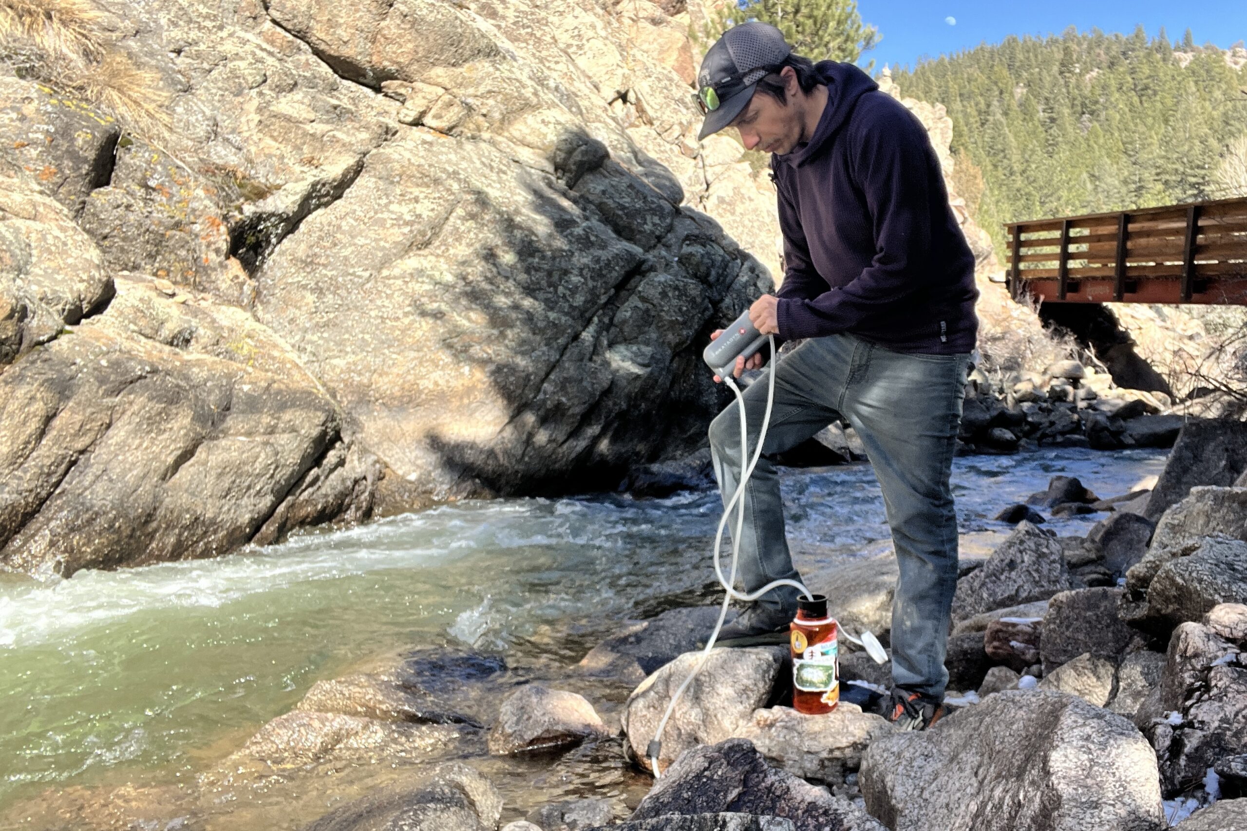 A hiker stands next to a creek and pumps water into a nalgene with the katadyn hiker filter.