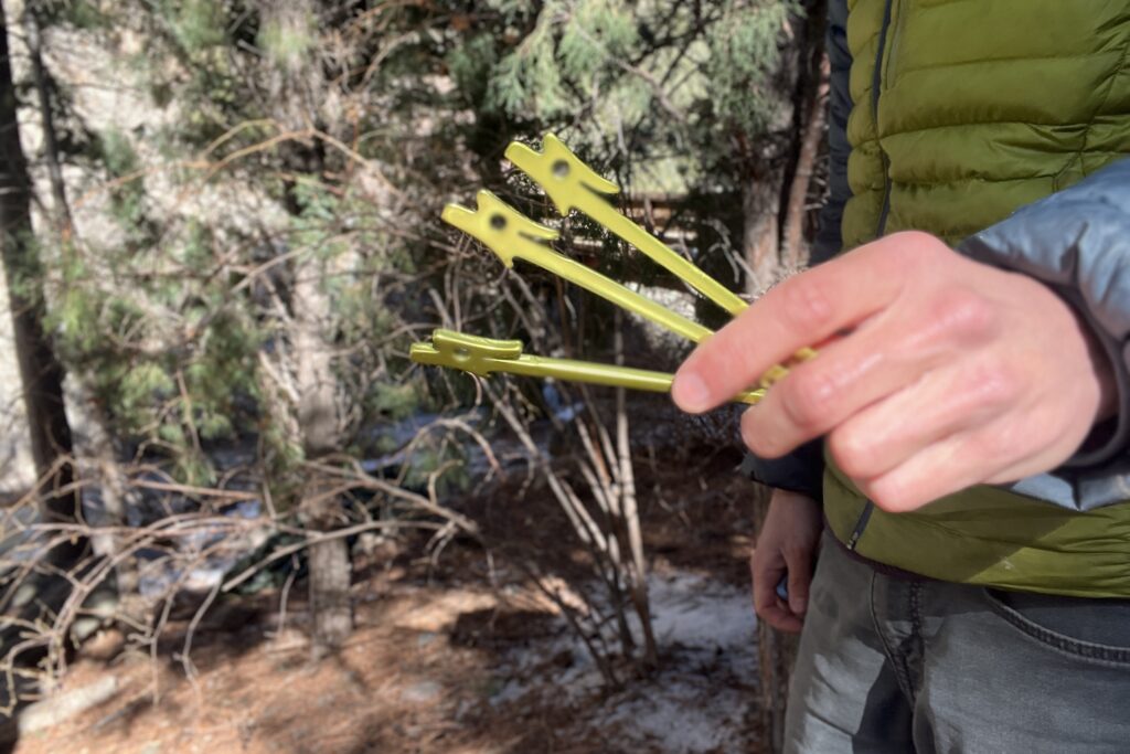 A hiker holds three green tent stakes in his hand.