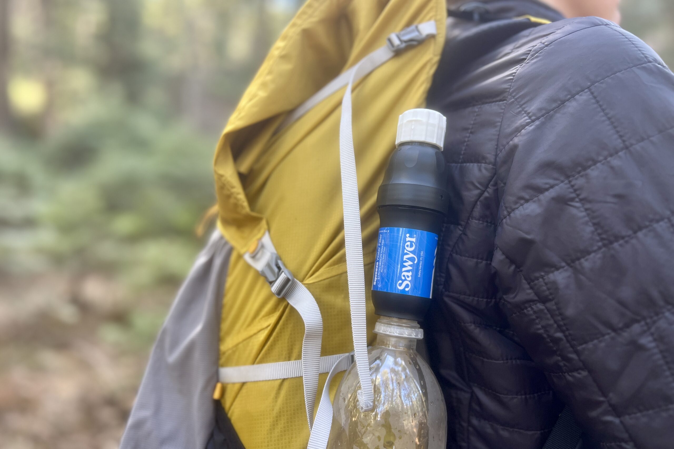 A hiker wears a backpack with the sawyer squeeze attached to a smartwater bottle in the side pocket.
