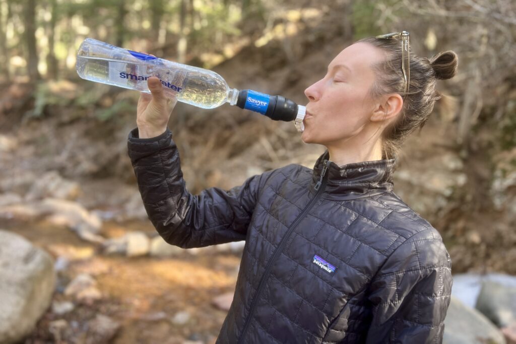 A hiker drinks from the sawyer squeeze attached to a plastic bottle.