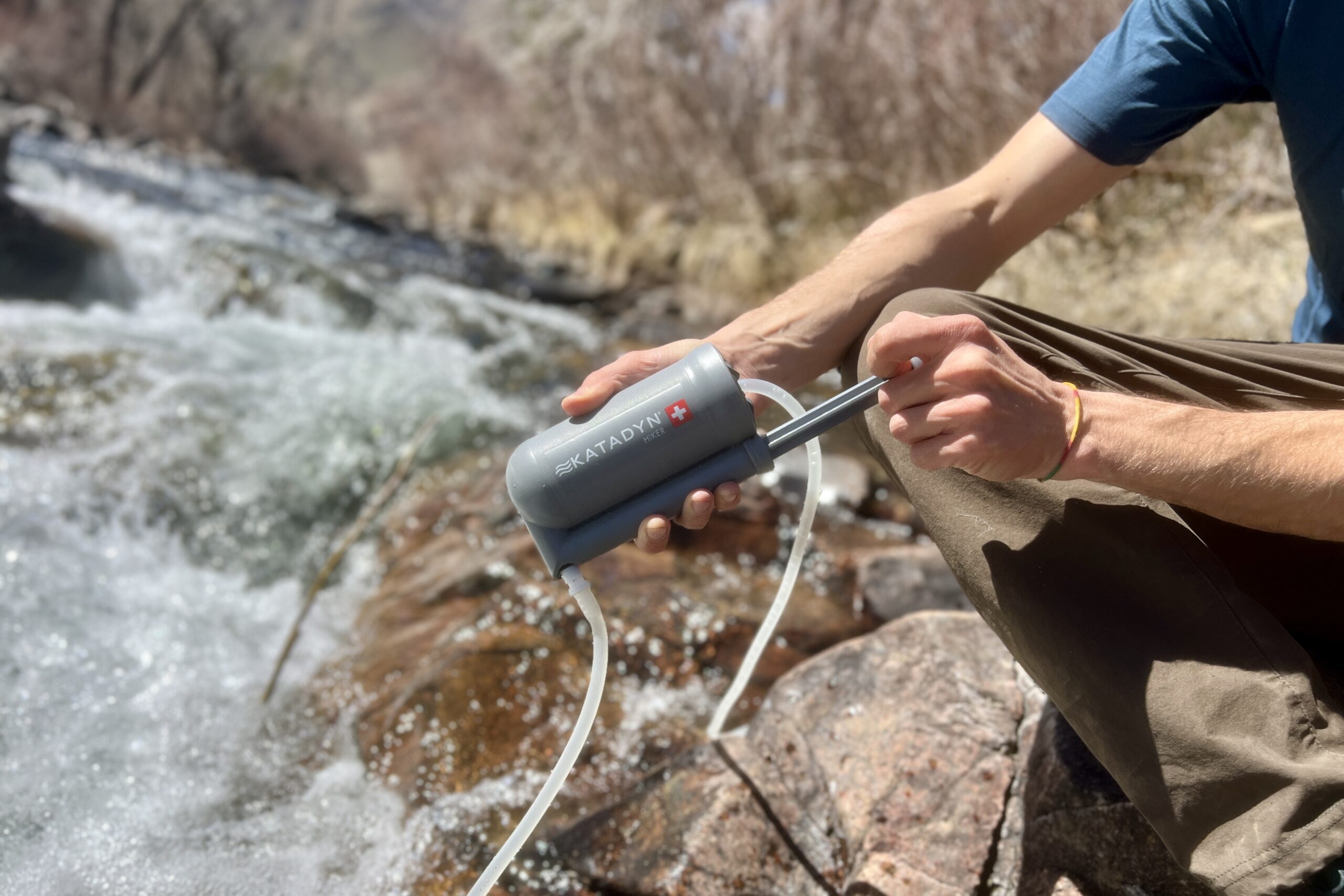 A close up of a hiker pumping water next to a creek with a hand pump filter