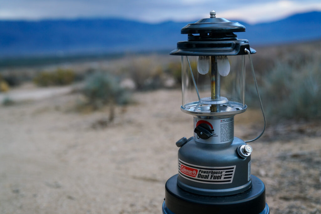 The Coleman Powerhouse Dual Fuel lantern sits unlit with desert and a mountain ridgeline in the background.