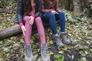 two people sitting on a log, one in blue leggings and one in pastel pink leggings. close-up on just the bottom half. person wearing pink leggings is touching the fabric