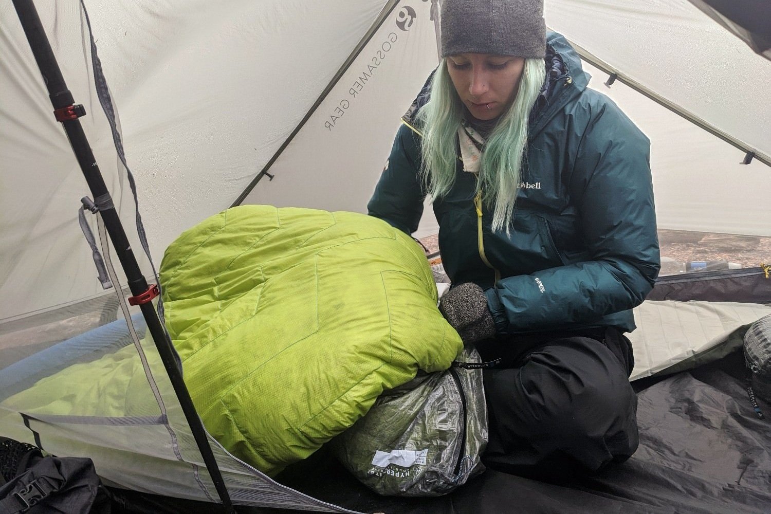 a backpacker in their tent stuffing their sleeping bag into a stuff sack 