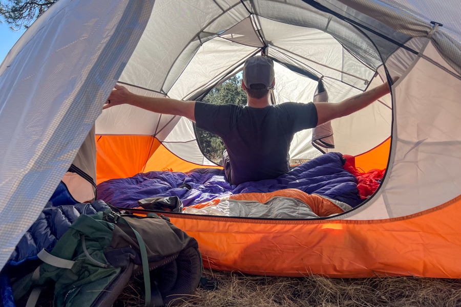 A man stretches his arms inside a tent to showcase how roomy the tent is.
