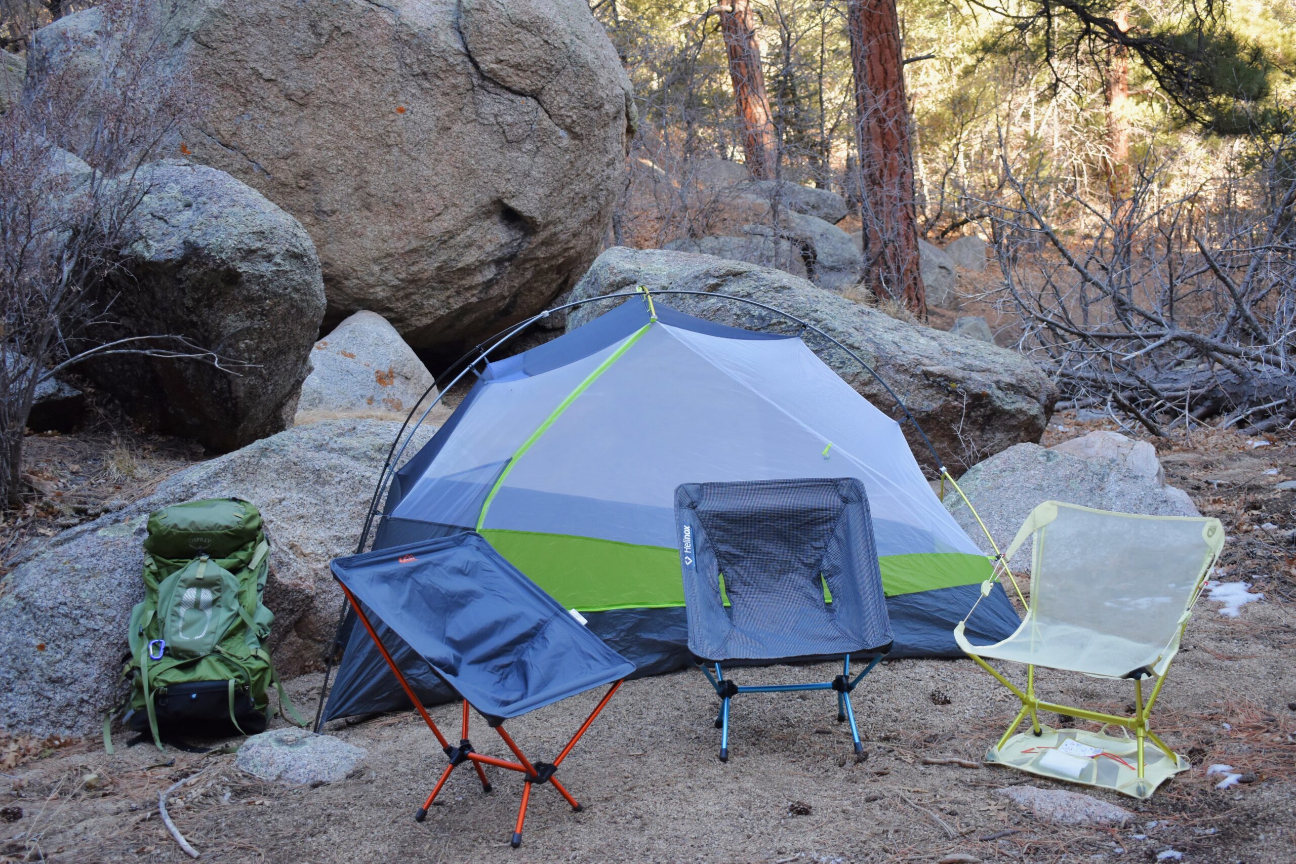 3 ultralight backpacking chairs are lined up next to each other in front of a test at a campsite with house-sized boulders behind it