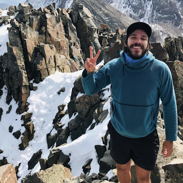 A smiling man flashes a peace sign on top of a snowy mountain.